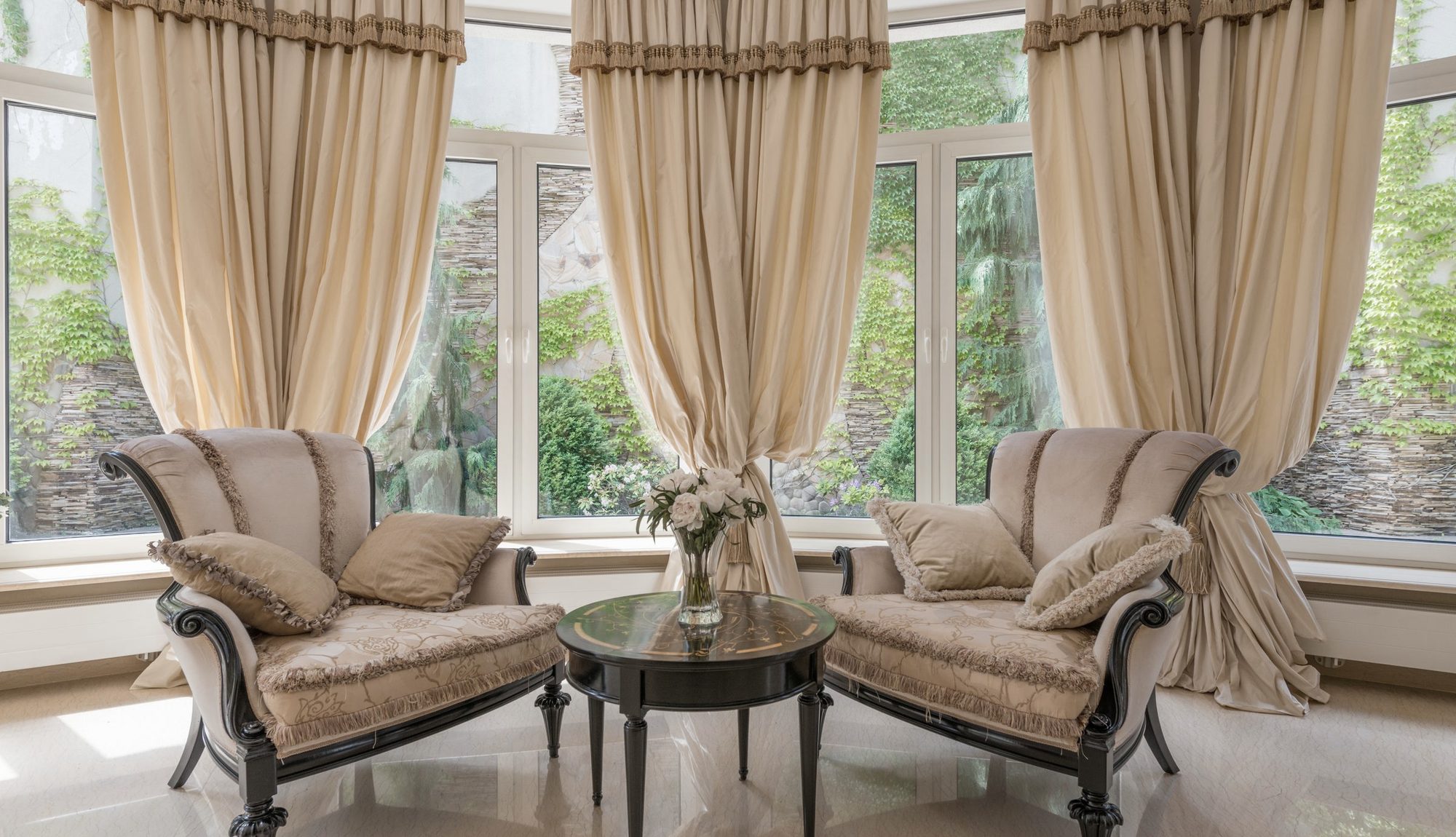 A light-filled living room with a low table, flowers and tall windows